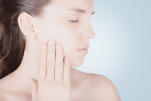 Woman with jaw pain holding her cheek and frowning.